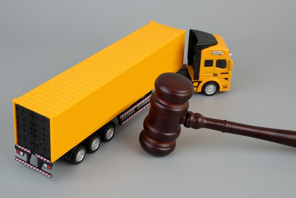 Wooden judge gavel and yellow cargo truck on grey background.