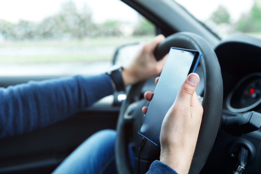 Driver using a smartphone behind the wheel illustrating distracted driving risks and liability in Uber and Lyft accidents in Florida